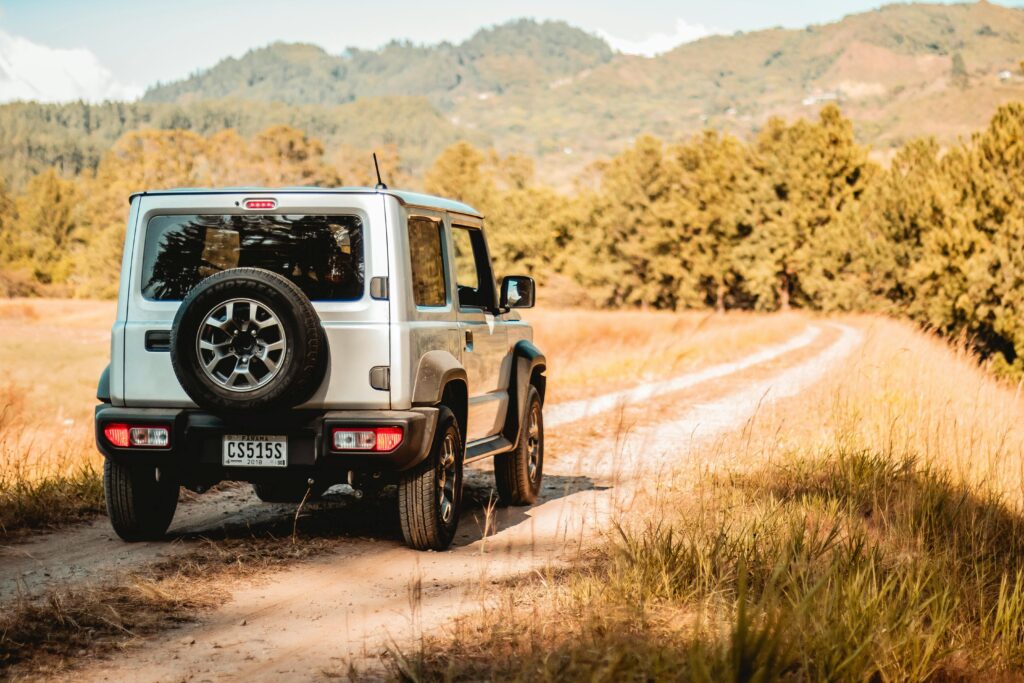 An off-road vehicle driving through a picturesque countryside path with mountains in the background.